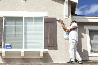 Peintre repeignant la façade et les encadrements d'une maison